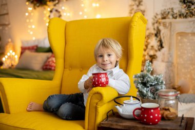 Tatlı çocuk, oğlum, Noel için süslü bir odada sarı bir koltukta oturuyor, rahat bir yer.