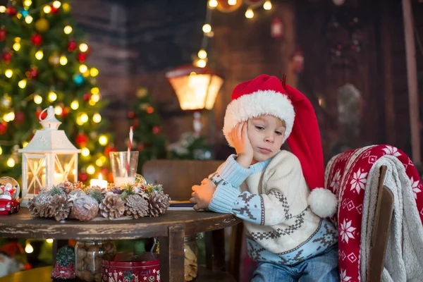 かわいい幼児の子供 クリスマスの服の少年 クリスマスの木製キャビンで遊んで 彼の周りの装飾 児童書やお茶を飲む — ストック写真