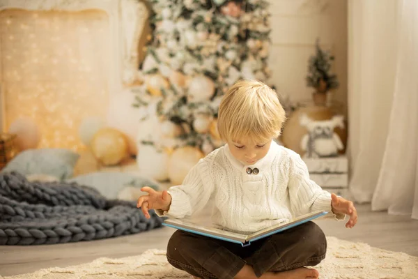 かわいいブロンドの幼児の就学前の男の子 本を読んで 居心地の良い家 ライトと装飾にクリスマスにプレゼント — ストック写真