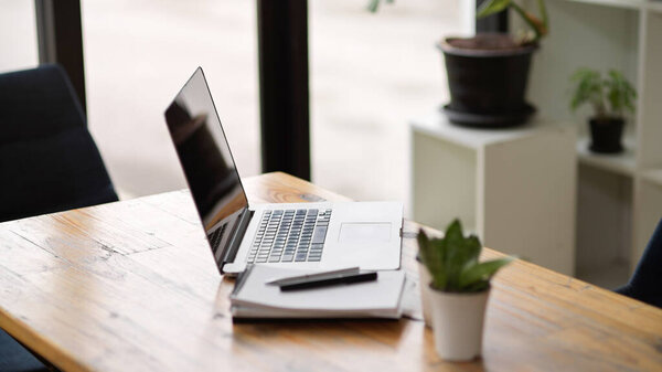 Боковой вид открытого портативного ноутбука на деревянный стол с ноутбуками и декором в современном и уютном офисе 
