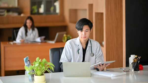 若い男性の医者はノートパソコンを使っている 病院では男性医師が手術計画を読み ノートパソコンで医学研究を行う — ストック写真