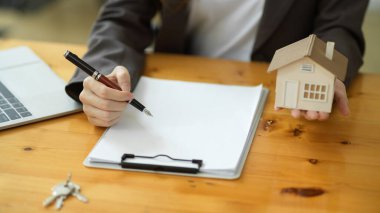 Kadın bir emlakçı kira sözleşmesi hazırlıyor ve bir ev modeli tutuyor. kırpılmış atış