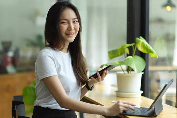 漂亮的年轻亚洲女人 手里拿着手机和笔 桌上放着平板电脑 — 图库照片