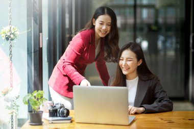 Birlikte dizüstü bilgisayar kullanan, online projeyi tartışan, modern bir ofiste cihaz ekranına bakan iki bayan meslektaşım.