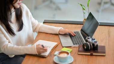 Kırpılmış görüntü, Millennial kadın serbest internet blogcusu kitabına başlık listesini yazarken kafede dizüstü bilgisayar üzerinde çalışıyor..