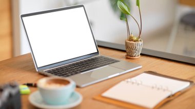 Modern dizüstü bilgisayarı boş ekran maketi, boş defter ve ahşap masa dekorasyonu ile yakın plan stil çalışma alanı.