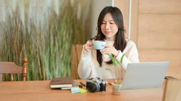 美しいコーヒーショップに座っている若い女性は 午前中にホットコーヒーを飲んで ラップトップコンピュータ上で仕事の後に休憩を取る — ストック写真