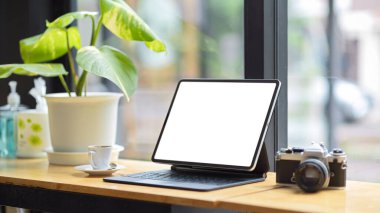 Tablet bilgisayar boş ekran modeli, antika retro kamera, kahve fincanı, kapalı masa bitkisi bulanık arka plan