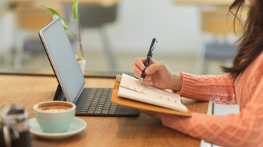 Çevrimiçi sınıfında okuyan ve not defterindeki önemli konuları anlatan bayan üniversite öğrencisinin yan görüntüsü.