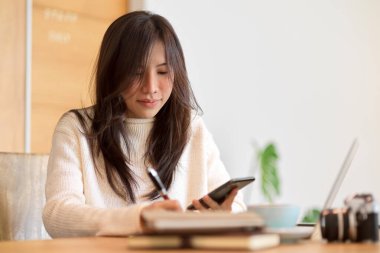 Mobil ekrana bakarken notlar alan güzel bir üniversite öğrencisi..