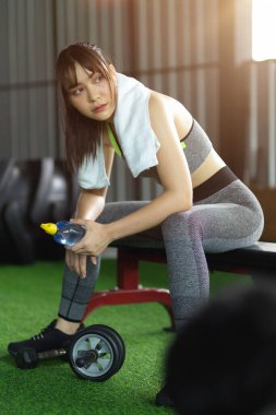 Çekici genç fitness kızı spor aletlerinin üzerine su şişesiyle oturur. Sıkı çalışmadan sonra biraz dinlen.. 