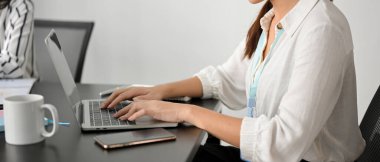 Dizüstü bilgisayarında çalışan, klavyede yazan, ofiste oturan sıradan bir kadın iş adamının kırpılmış görüntüsü..