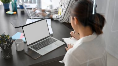 Ofiste kağıda notlar yazarken dizüstü bilgisayarda çalışan kadın pazarlama görevlisi. dizüstü bilgisayar boş ekran modeli.