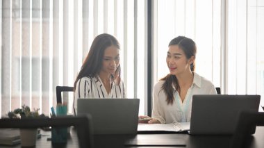 İki iş arkadaşı modern, parlak bir ofiste dizüstü bilgisayarla iş birliği yapıyorlar..