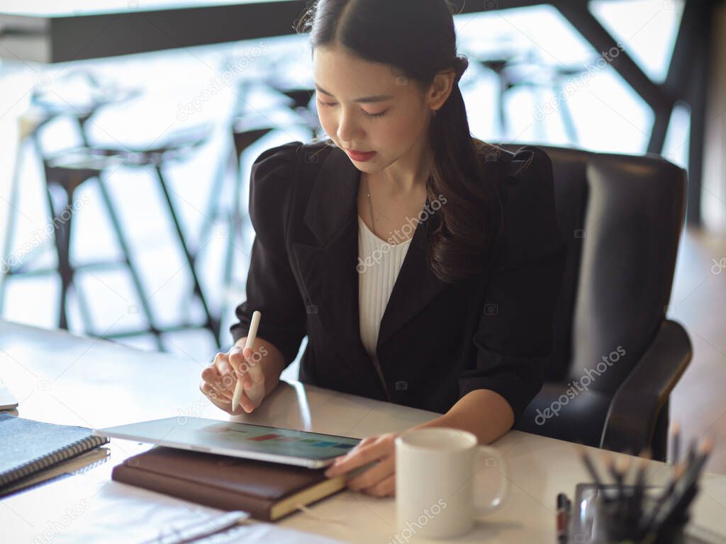Portrait of beautiful young businesswoman working at her desk, making decision while looking at the informations on tablet.