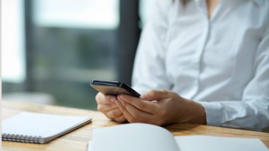 Yakın plan, akıllı telefon kullanan, okuyan ve iş e- postalarına cevap veren kadın asistan.