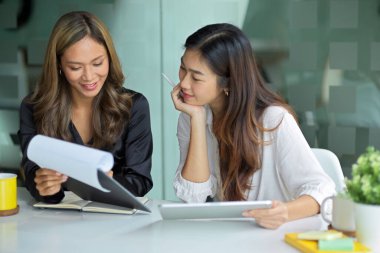 Mutlu iş kadınları evrak işleri hakkında bilgi okuyor ve modern ofiste süreç hakkında sohbet ediyorlar.