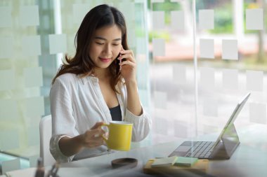 Genç ve güzel Asyalı bir serbest yazar, kahve dükkanında çalışıyor ve telefonda konuşuyor.