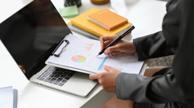 Masasındaki veri tablosunda kadın yöneticinin mali tablosunu kontrol ederken çekilmiş görüntüsü..