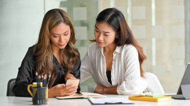 Bayan meslektaşlar taşınabilir bir uygulama kullanarak yemek siparişi vermeye karar verirler, yemek uygulamalarına doğru kaydırırlar ve akıllı telefon ekranına bakarlar..