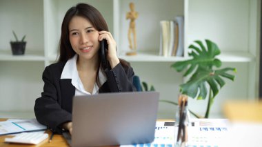 Asyalı genç bir bayan işçi telefonda konuşuyor, ofiste işleri tartışıyor..