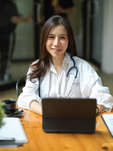一位快乐的亚洲女医生的肖像坐在办公室的工作台上 在平板触摸屏上工作 — 图库照片