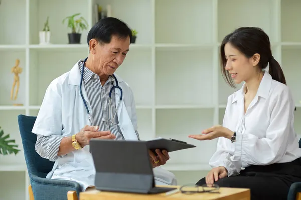 一名亚洲女病人在健康中心向一位中年专科医生咨询她的伤害计划 — 图库照片