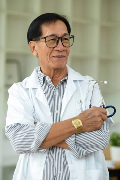 一位成功的亚洲中年男性治疗师 戴着眼镜 身穿白色长袍 双臂交叉地站在诊所里 — 图库照片