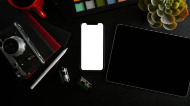 Üst manzara, düz yatış. Modern cihazlı modern çalışma alanı, akıllı telefon boş ekran, tablet, siyah arka planda retro kamera