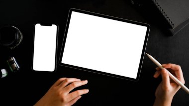 Dijital tablet bilgisayarda kadın eli çiziminin üst görüntüsü. Siyah arkaplanda tablet ve akıllı telefon boş ekran. düz yat