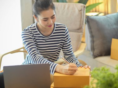 Bir internet mağazasının kadın sahibi bir paket kutusuna müşterinin adresini yazar. sevkiyat, posta, küçük işletme, e-ticaret konsepti.