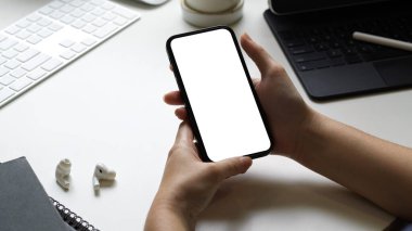 Kadın elleri arka planda modern çalışma alanı olan boş ekran akıllı telefonu tutuyor.