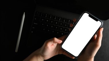 Yakın plan, modern karanlık çalışma masasında akıllı telefon boş ekran maketi tutan bir kadının elleri..