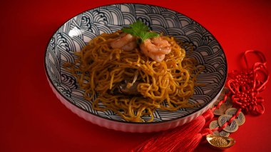 Porselen tabakta karidesli Chow mein veya Hakka noodle ve kırmızı arka planda Çin şans tılsımları..