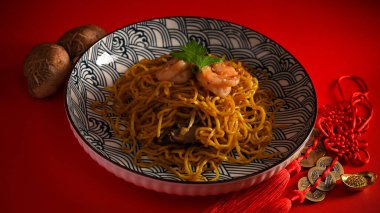 Porselen tabakta karidesli Çin yemeği, mantar ve kırmızı arka planda Çin şans tılsımı..