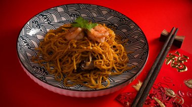 Karidesli Çin yemeği ya da Çin usulü kızarmış erişteli karides tabağında karides ve kırmızı arka planda çubuk. Çeviri: 