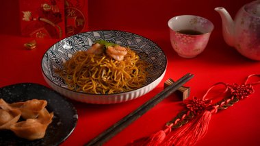 Kırmızı yemek masasında karidesli kızarmış sarı erişte ve kızarmış hamur köftesi. Çin mutfağı.