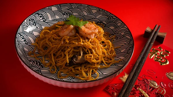 Karidesli Çin yemeği ya da Çin usulü kızarmış erişteli karides tabağında karides ve kırmızı arka planda çubuk. Çeviri: 