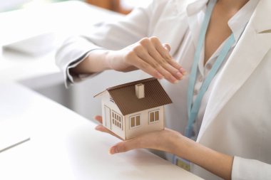 İş kadını ya da emlakçı kadın ofis masasında bir ev mankeni tutuyor. konut yatırımları.