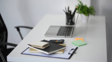 Taşınabilir dizüstü bilgisayarı olan bir çalışma alanının yan görüntüsü ve beyaz masadaki ofis malzemeleri.