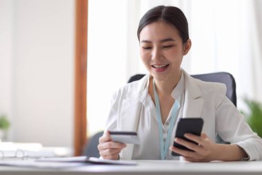 Masada akıllı telefon ve kredi kartı tutan Asyalı genç iş kadını ya da girişimci. Kredi kartı konsepti olan iş adamları. Mobil bankacılık, online alışveriş veya para transferi.