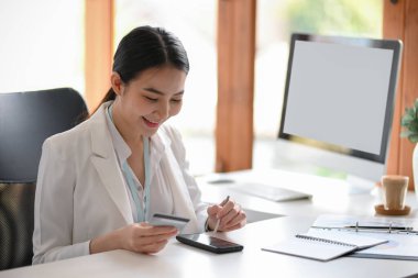 Kadın yönetici ya da girişimci, faturalarını ödemek için mobil bankacılık uygulamasını kullanarak modern ofiste oturuyor. Akıllı telefonlu kredi kartı.