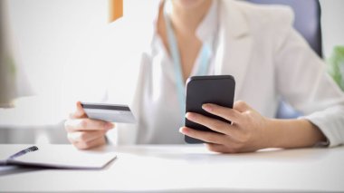 Bir iş kadınının kırpılmış görüntüsü internetten alışveriş yapıyor ve mobil bankacılık başvurusuna para ödüyor. Akıllı telefonu ve kredi kartı olan bir kadın..