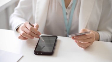 Bir kadın işçinin ya da iş kadınının akıllı telefonlu stilus kalem kullanırken çekilmiş görüntüsü, cep telefonu uygulamasına bağlanmak için elinde kredi kartı var. Çevrimiçi ödeme kavramı.