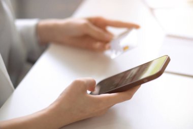 Yakın plan, modern bir akıllı telefon ve kredi kartı bir kadının elinde. Mobil bankacılık hizmeti, dijital çevrimiçi ödeme kavramı.