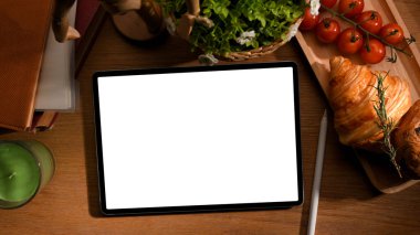 Çalışan masa konseptiyle ilgili kahvaltılı dijital tablet. Kruvasan, ahşap tabakta domates.