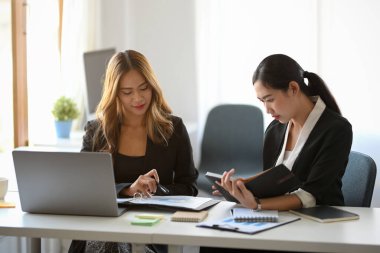 Ofiste asistanıyla çalışan çekici bir Asyalı kadın yönetici. Yöneticiyle görüşürken not alan bayan asistan.