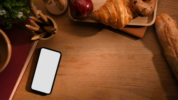 Akıllı telefon beyaz ekran maketi, kahvaltı seti, kırtasiye malzemesi ve ahşap arka planda grafik görüntüleme alanı olan bir çalışma alanı. en üstteki görünüm