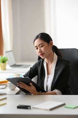 Female manager or business entrepreneur reading the informations on a clipboard paper at her workspace.