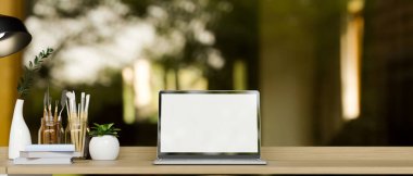 Simple workspace with laptop computer mockup, painting tools, decor on wooden table over blurred green forrest background. 3d rendering, 3d illustration